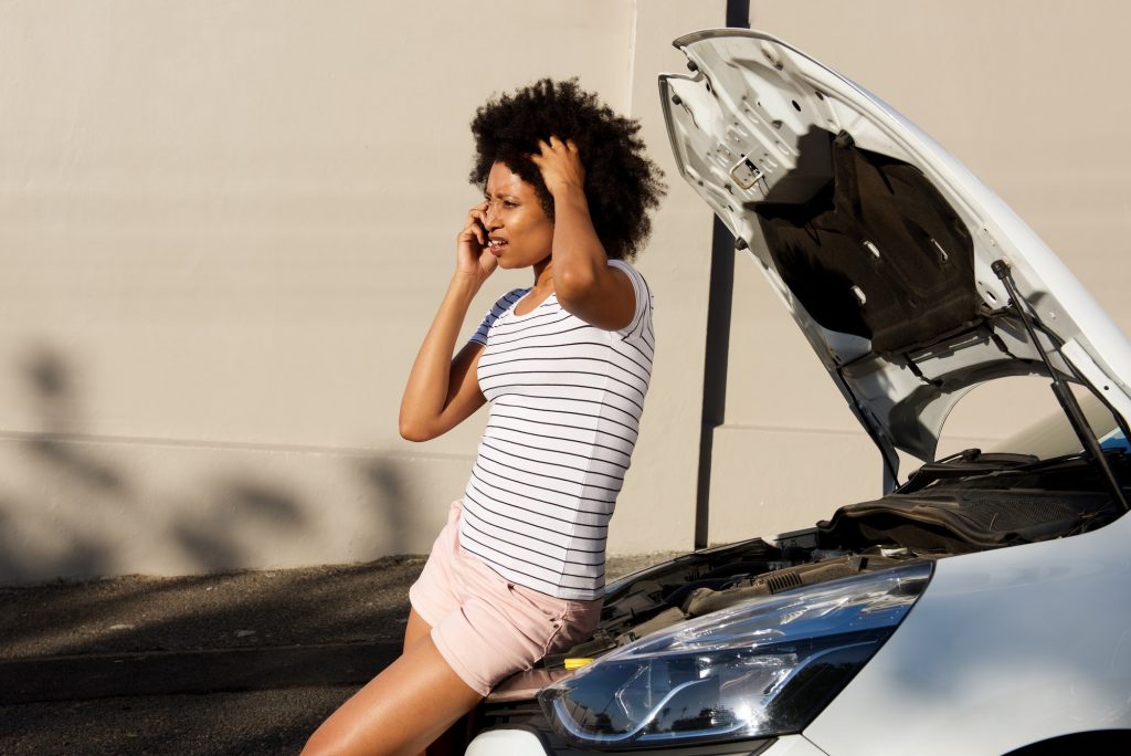 young woman standing by broken down car and making phone call for assistance